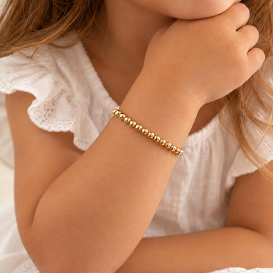 Gold-filled bead bracelet on a child’s wrist with a white ruffled dress
