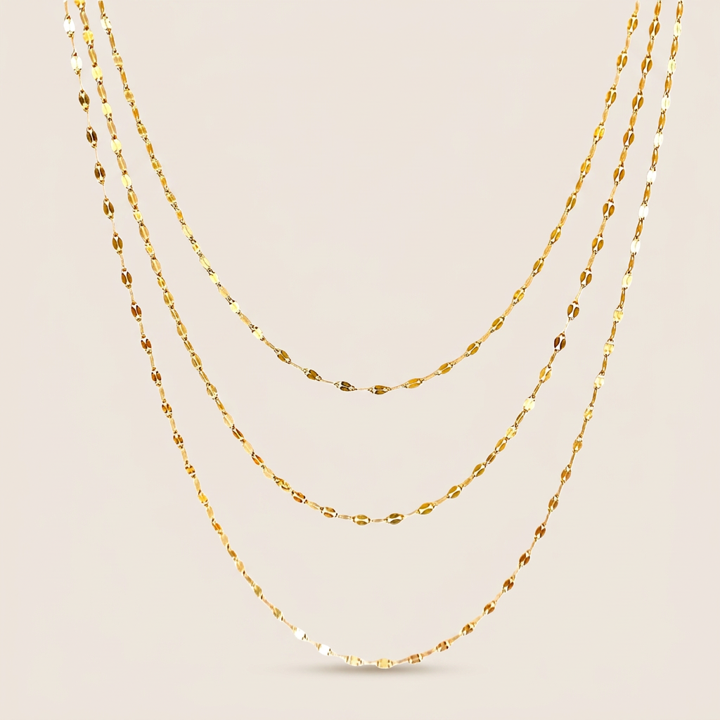 Three gold-filled mirror Valentino chain necklaces arranged in graduated layers on an ivory background