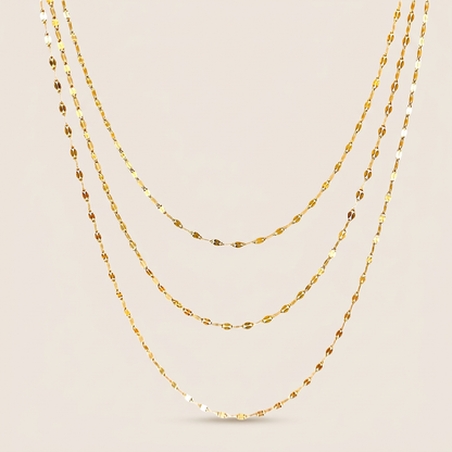 Three gold-filled mirror Valentino chain necklaces arranged in graduated layers on an ivory background
