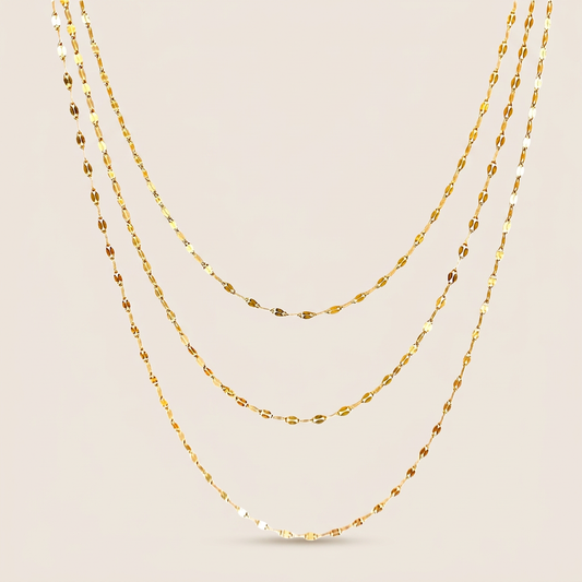 Three gold-filled mirror Valentino chain necklaces arranged in graduated layers on an ivory background