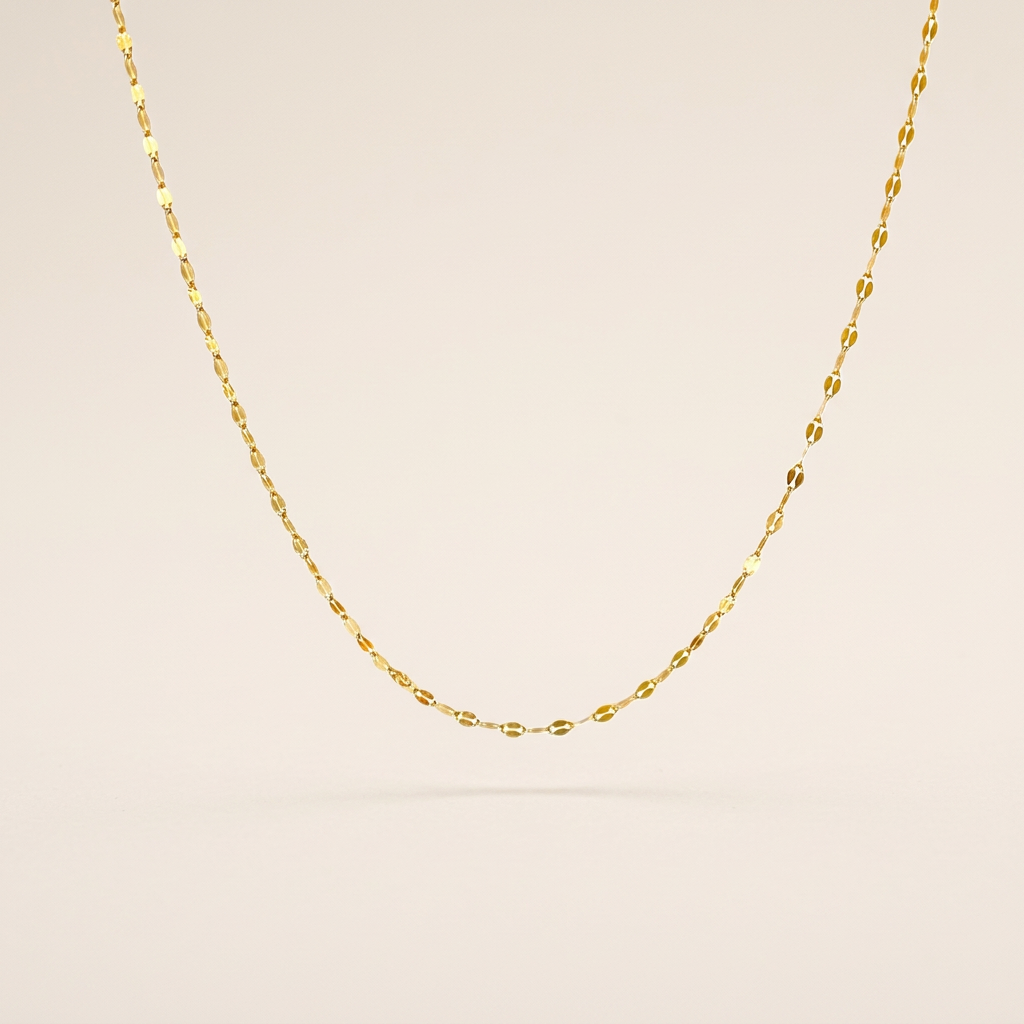 Single gold-filled mirror Valentino chain necklace arranged in a U shape on an ivory background