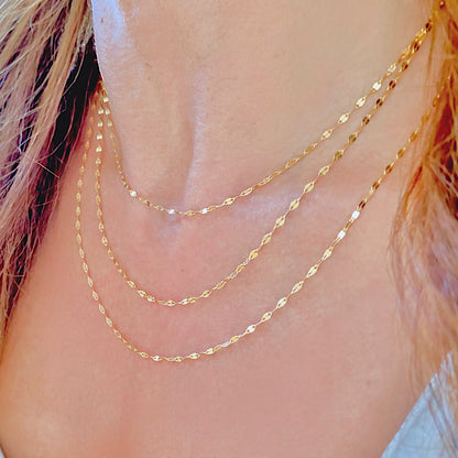 Close-up of three gold-filled mirror Valentino necklaces layered along the neckline