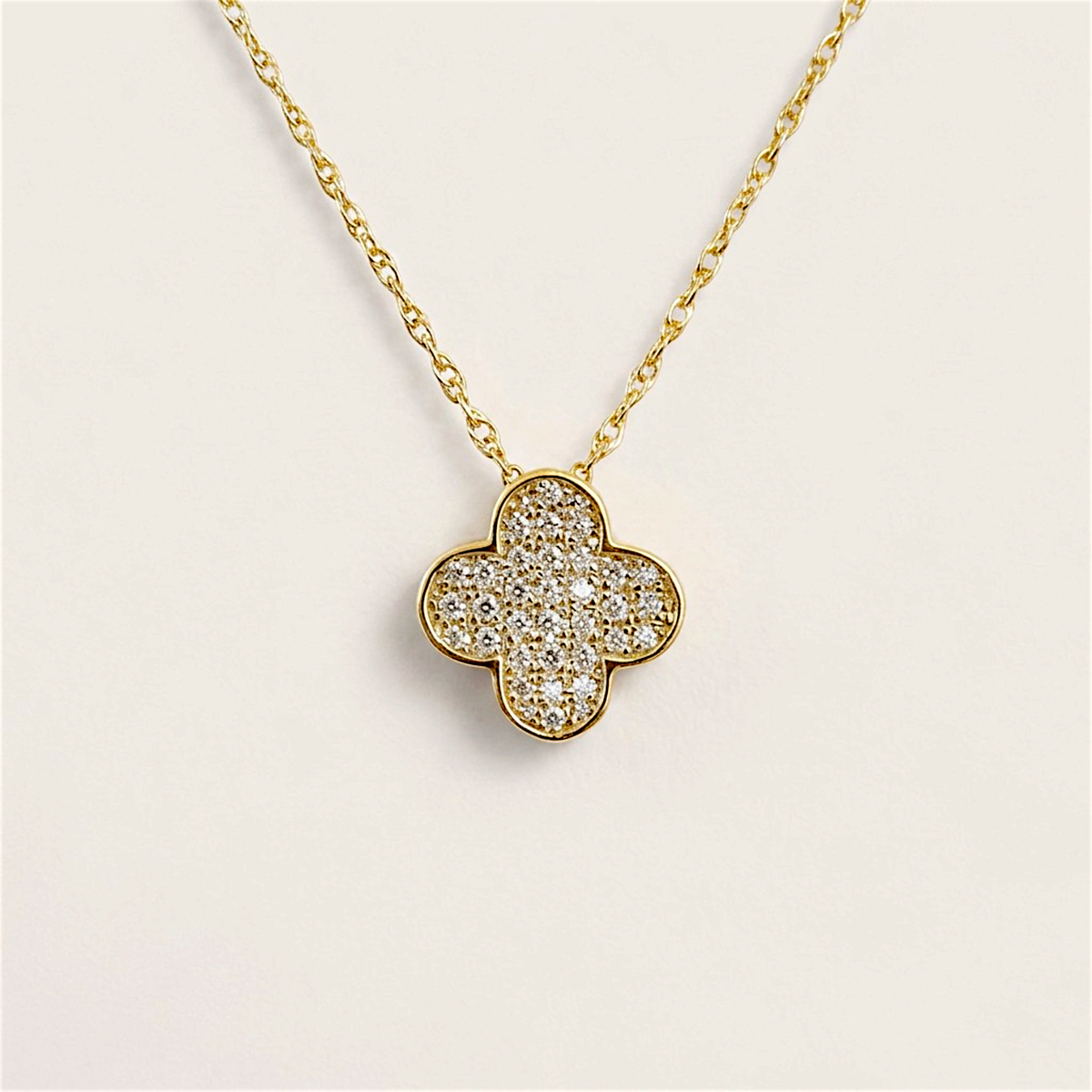 Front view of a diamond clover pendant with a polished yellow gold border and open rope linked chain on a warm neutral background