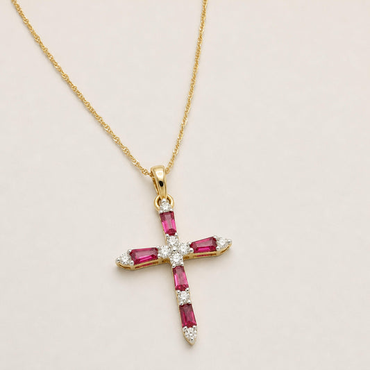 Ruby and diamond cross necklace in yellow gold, shown at a slight angle on a warm neutral background