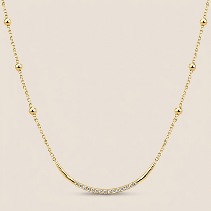 Yellow gold satellite necklace with round bead stations and a curved CZ-accented U-bar on a warm beige background
