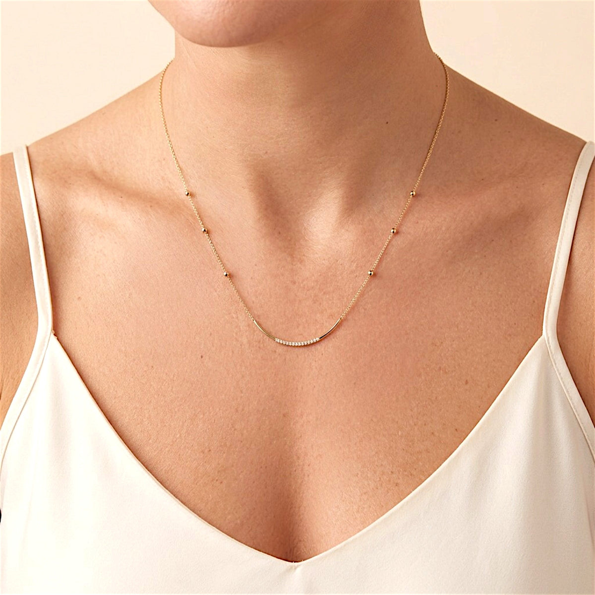 Gold bead-station necklace with a curved CZ bar worn at the neckline above an ivory camisole