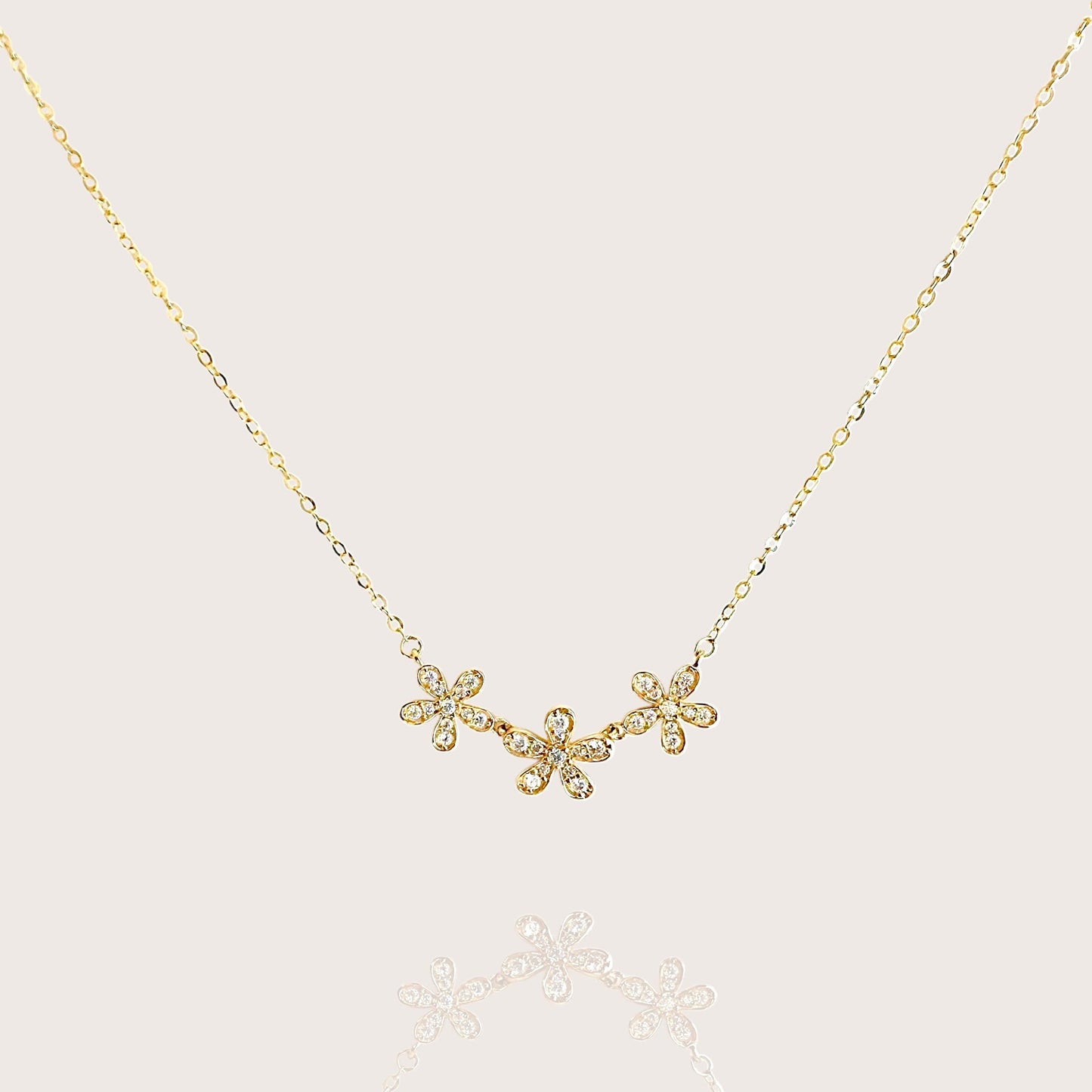 Product flat-lay of the solid 14k gold three-flower bar necklace by Ashley Nicole Jewelry, featuring three delicate floral clusters hand-set with sparkling simulated diamond cubic zirconia stones on an adjustable 16 to 18 inch gold rolo chain.