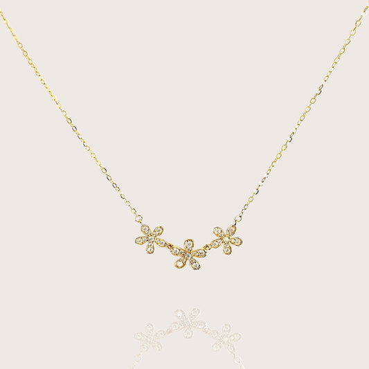 Product flat-lay of the solid 14k gold three-flower bar necklace by Ashley Nicole Jewelry, featuring three delicate floral clusters hand-set with sparkling simulated diamond cubic zirconia stones on an adjustable 16 to 18 inch gold rolo chain.