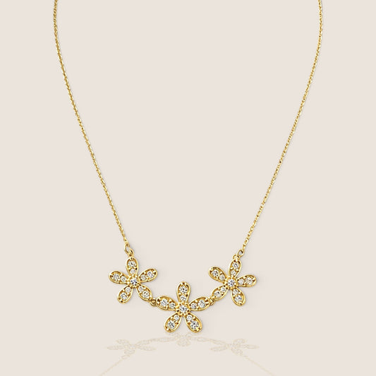 Yellow gold necklace with three connected five-petal CZ flowers and a fine chain on a warm beige background