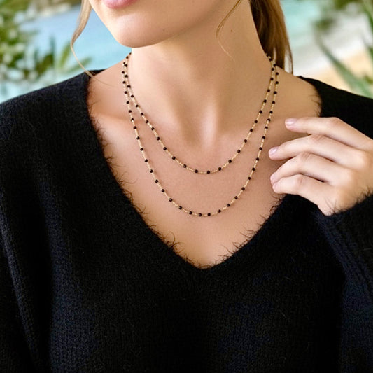 Model wearing  a 14K gold filled satellite black enamel beaded necklace layered in different lengths by Ashley Nicole Jewelry