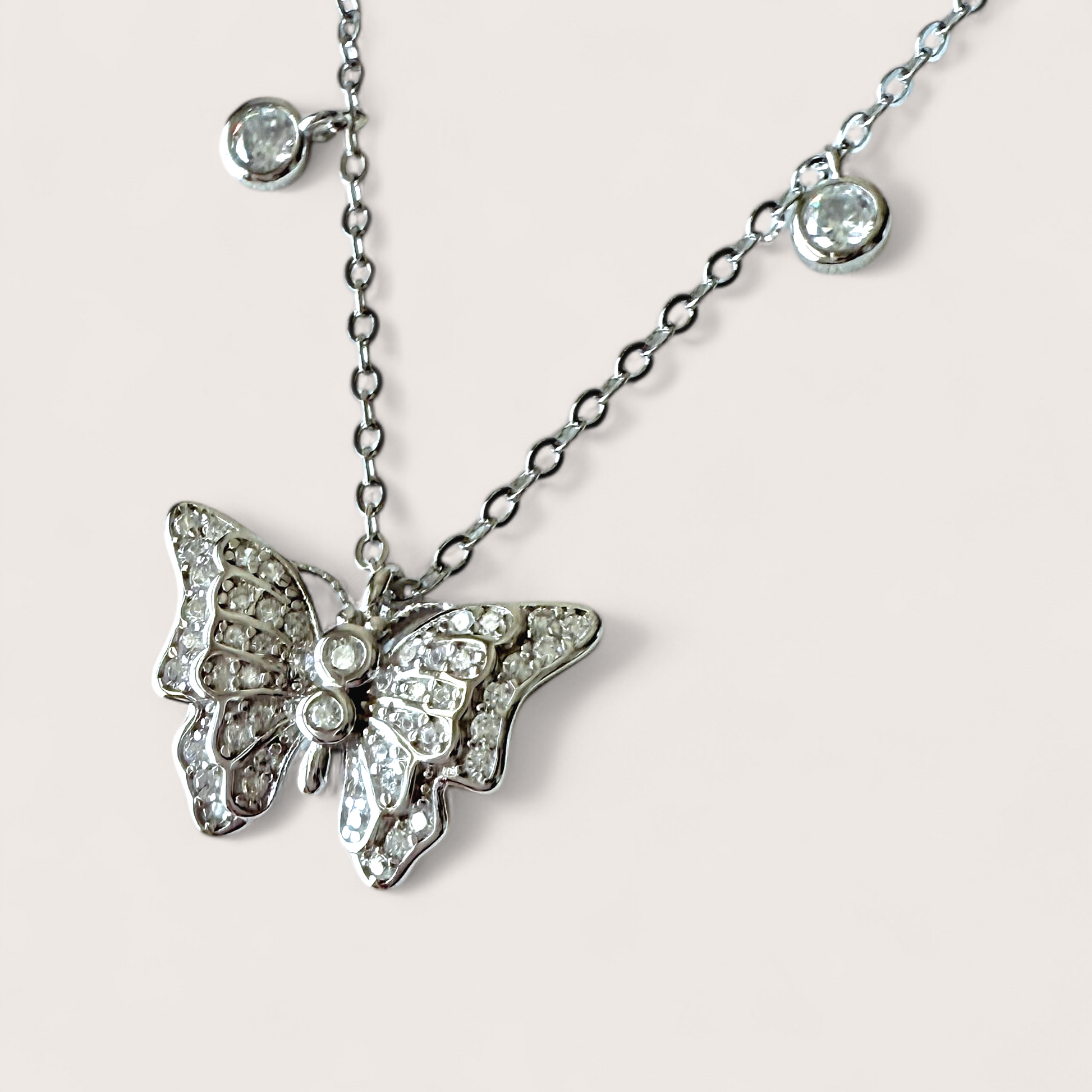Close up of butterfly and bezel charms on a rhodium sterling silver necklace with a 3D in-flight butterfly pendant adorned with dangling bezel set cubic zirconia gems,
