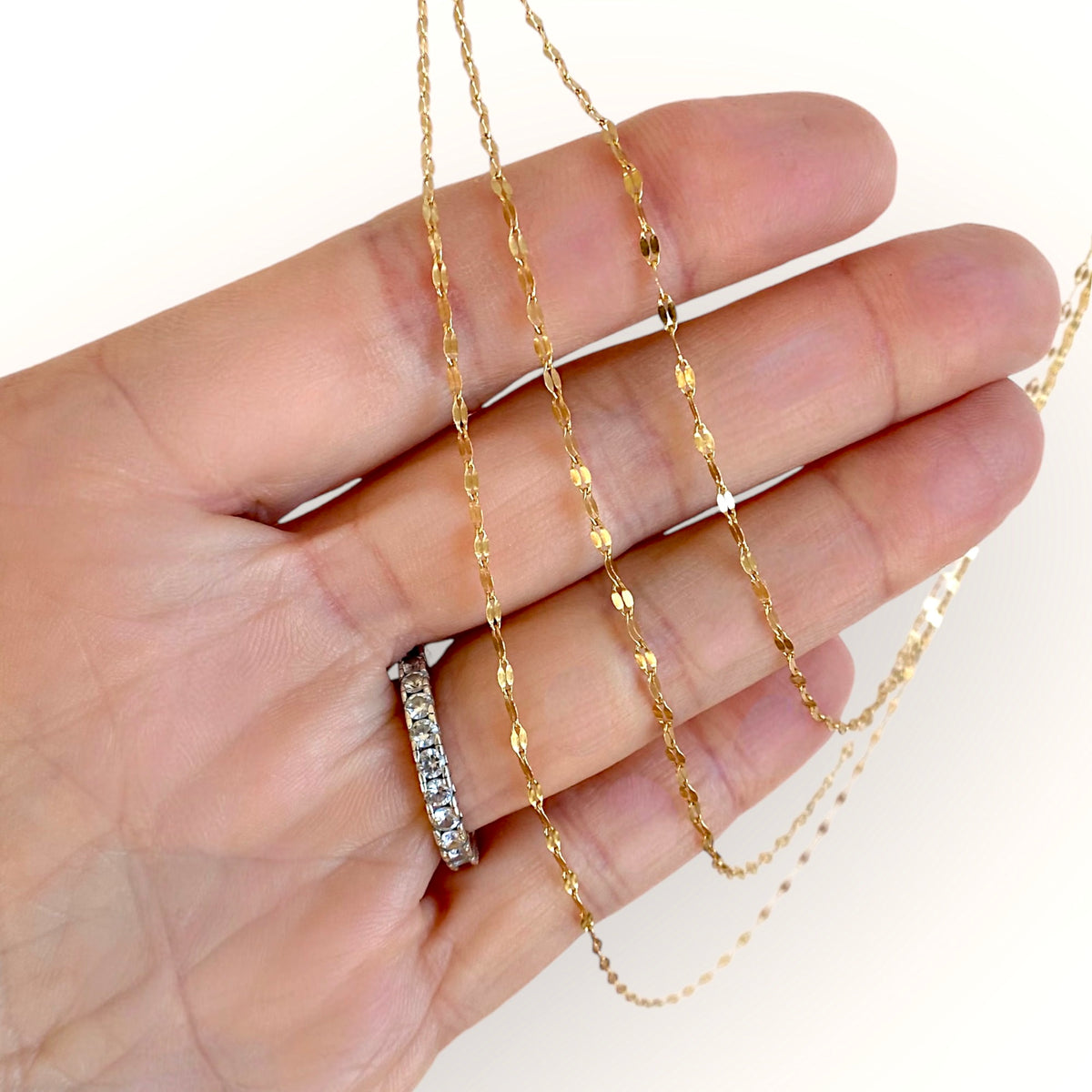Gold-filled mirror Valentino chains draped across a hand, showing the flat oval links
