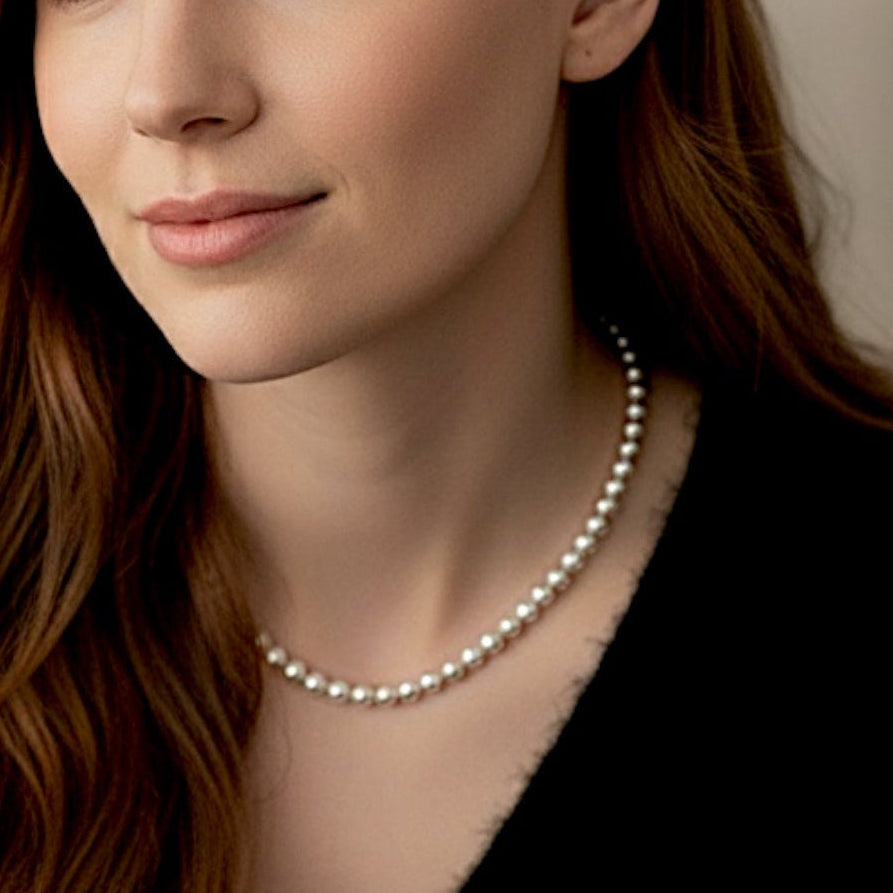 Close up of woman with red hair looking left, wearing a high-polish, solid 925 sterling silver 6mm round bead necklace over a black v-neck top against a warm minimalist studio background. The beads have a mirror-bright shine and are precisely scaled to 6mm