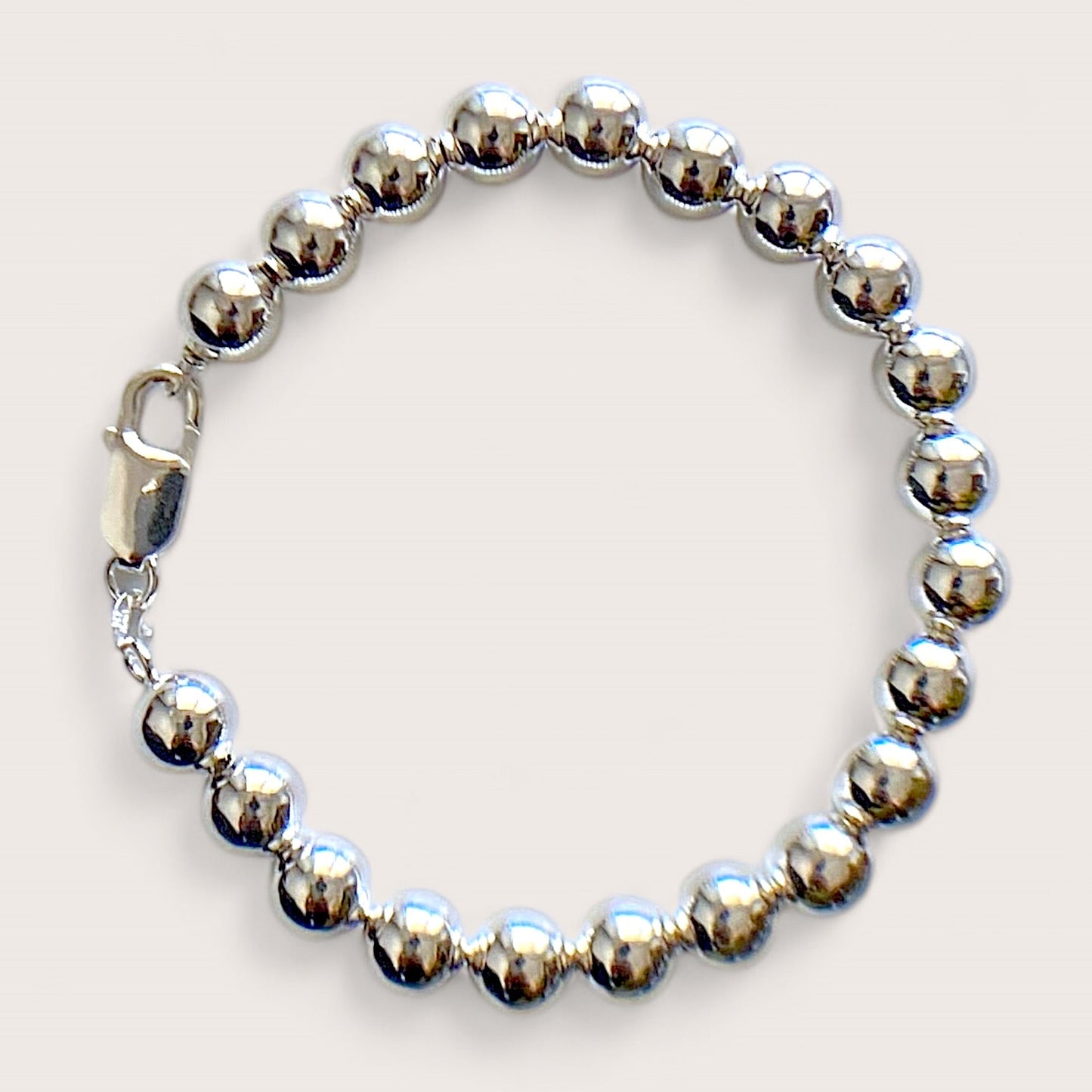 Close up of a polished 8mm sterling silver ball bead bracelet with a large lobster claw clasp on a white background by Ashley Nicole Jewelry