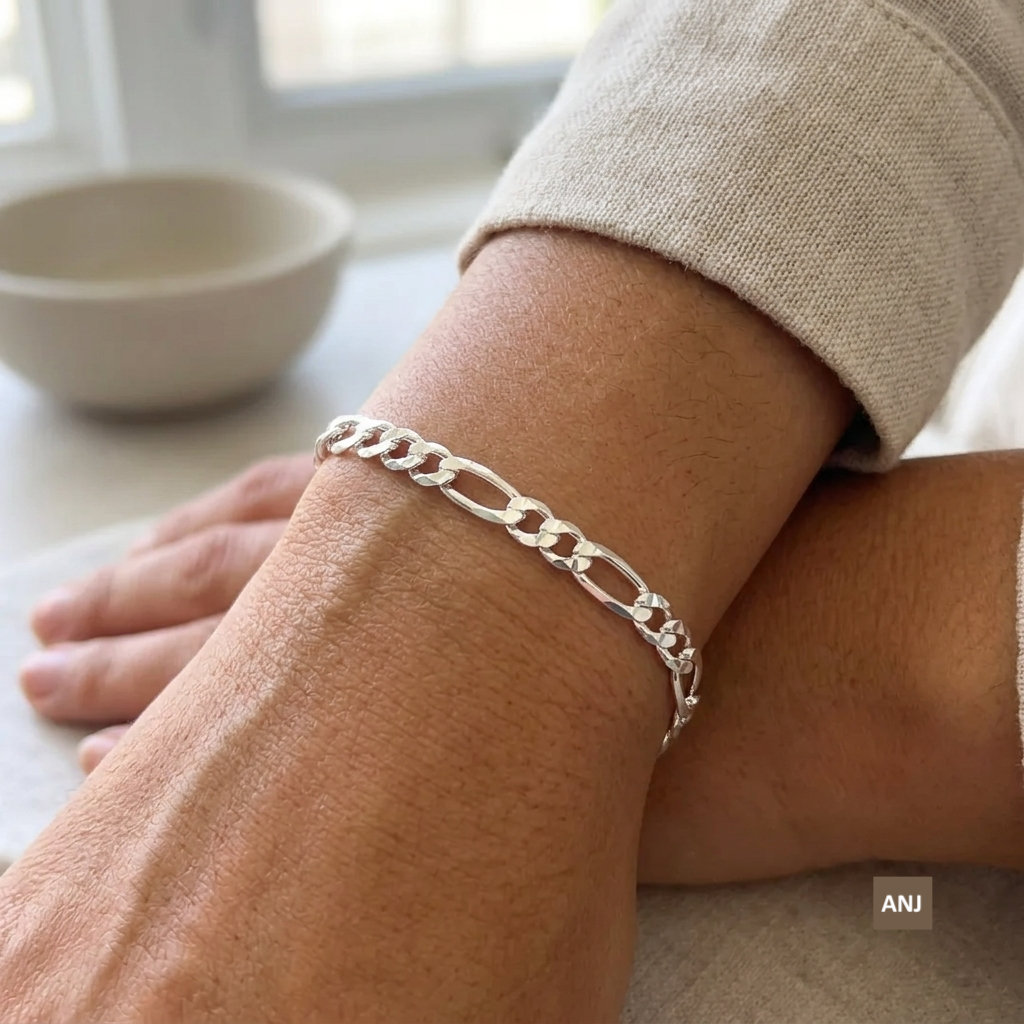 A close-up lifestyle shot showcasing the 4mm unisex sterling silver Figaro chain bracelet worn elegantly on a wrist, demonstrating how the links lay perfectly flat against the skin.