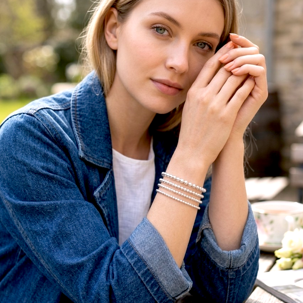 A woman wearing a stack of four silver beaded bracelets on her wrist,  925 sterling silver 2mm to 5mm stretch fit bracelet stack - by Ashley Nicole Jewelry 