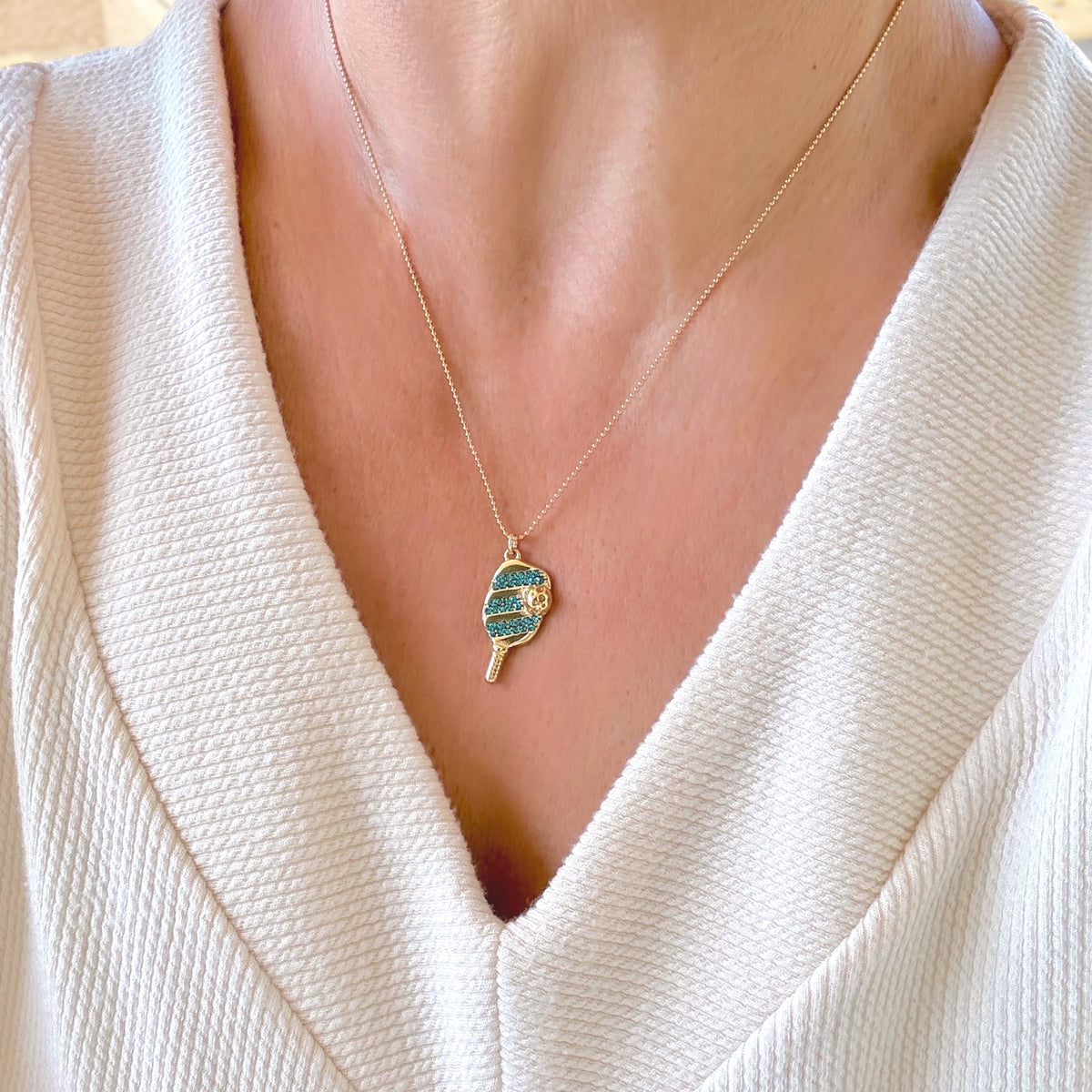 Model wearing the gold pickleball paddle necklace featuring blue pavé crystal accents.