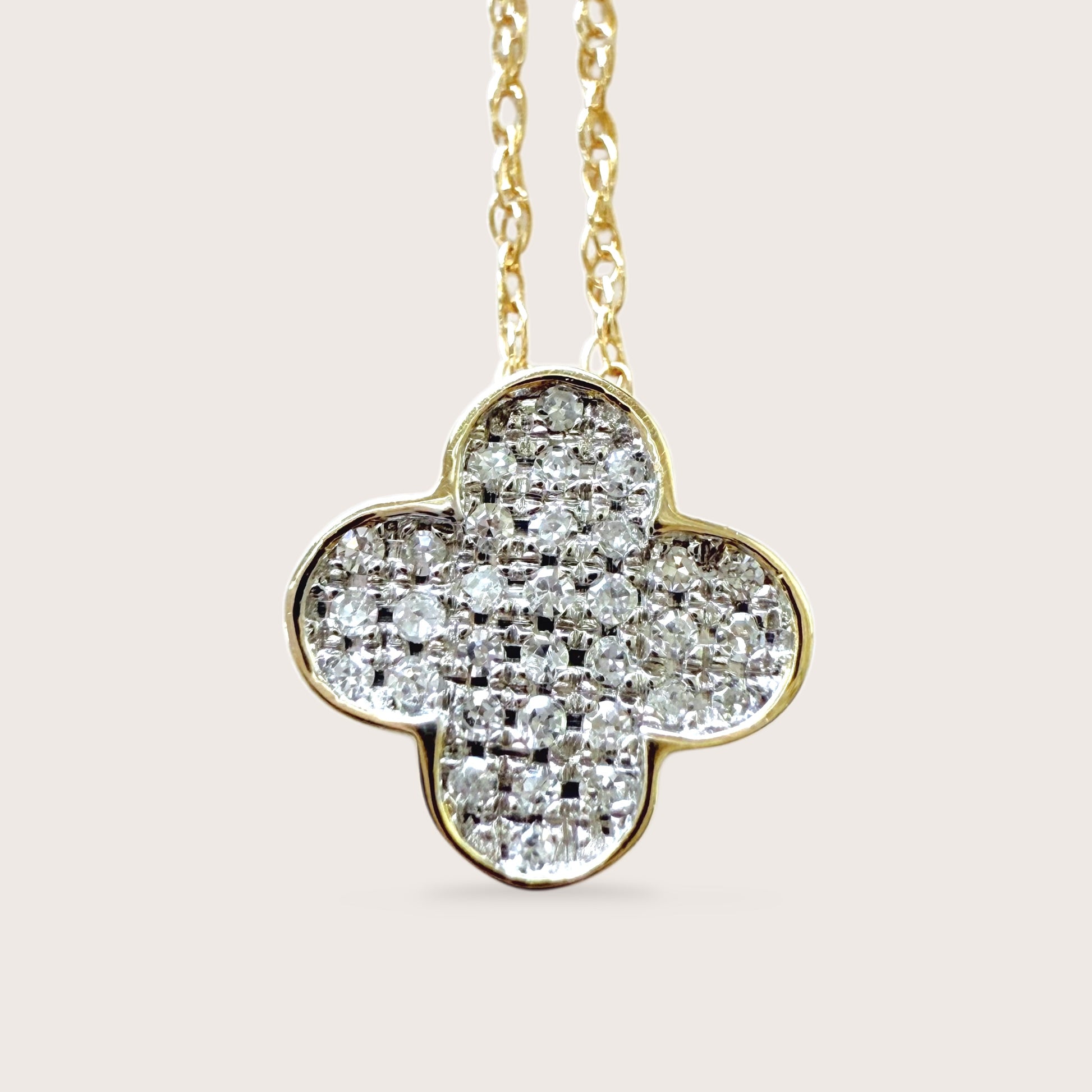 Diamond clover pendant on a gold chain against a light pink background