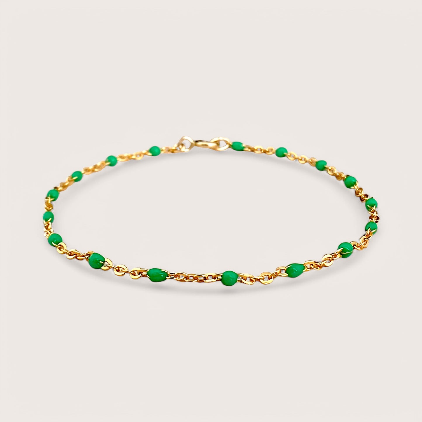 A dainty gold bracelet with emerald green enamel beads on a chain design, displayed against a plain background.