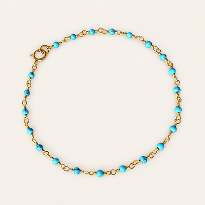Turquoise bead rosary chain bracelet with gold-plated links and a spring-ring clasp, arranged in a circle on a beige background.