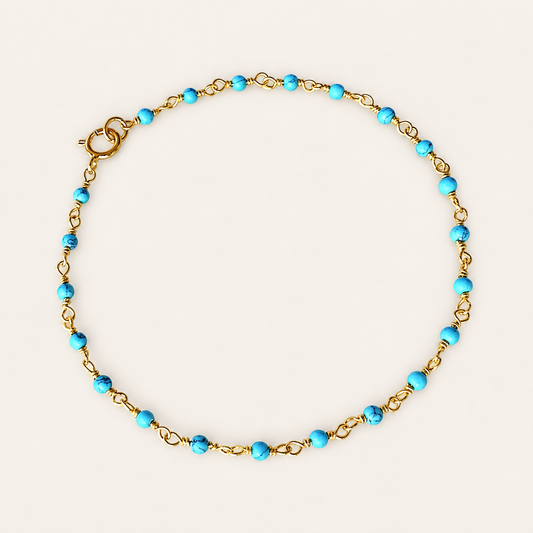 Turquoise bead rosary chain bracelet with gold-plated links and a spring-ring clasp, arranged in a circle on a beige background.