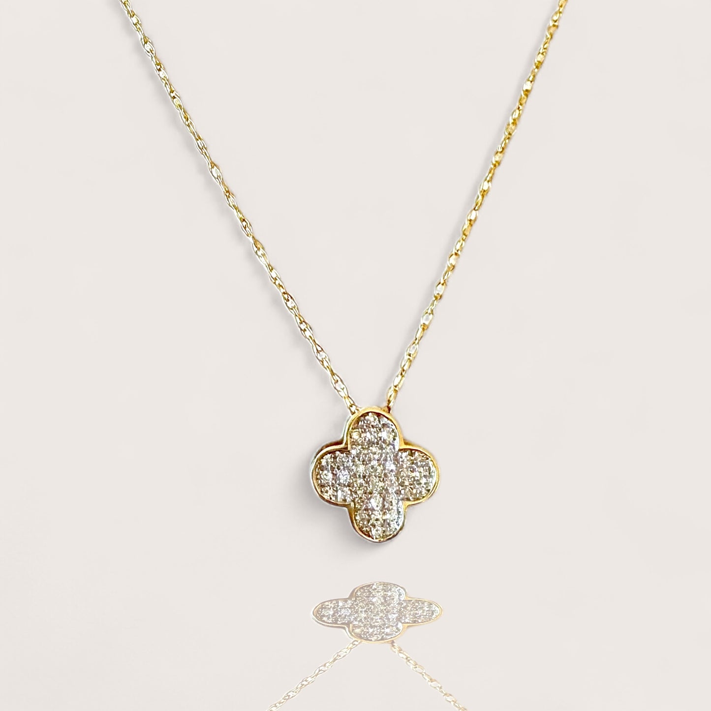 Gold necklace with a clover-shaped pendant on a light gray background