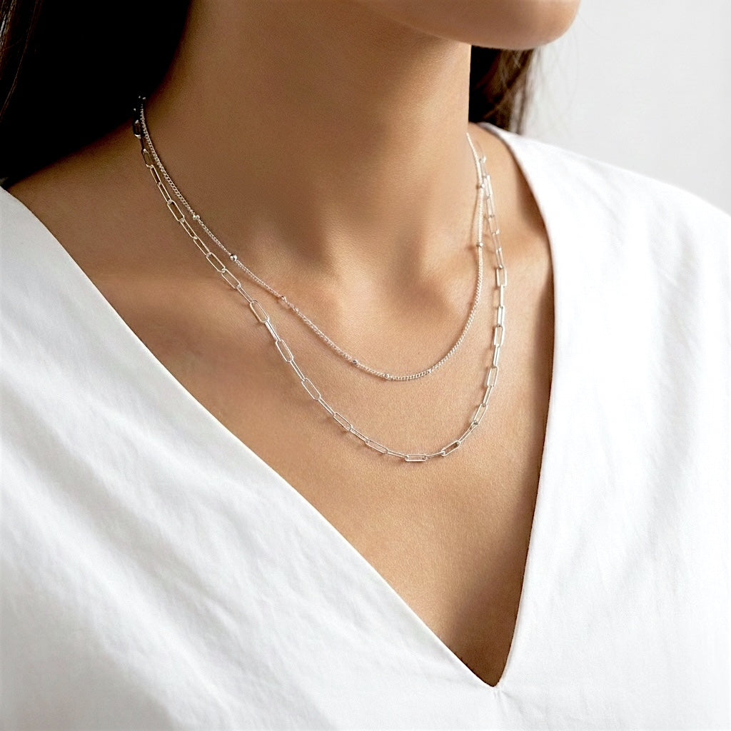 Modern minimalist jewelry styling: double-layered silver necklace with paperclip links and delicate beads on a female model