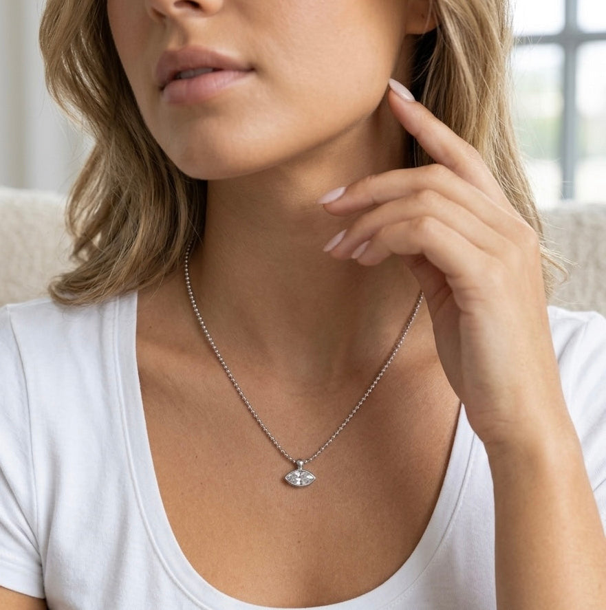 A close-up lifestyle shot of a woman wearing a delicate silver chain necklace with a small silver eye pendant, paired with a white scoop-neck t-shirt.