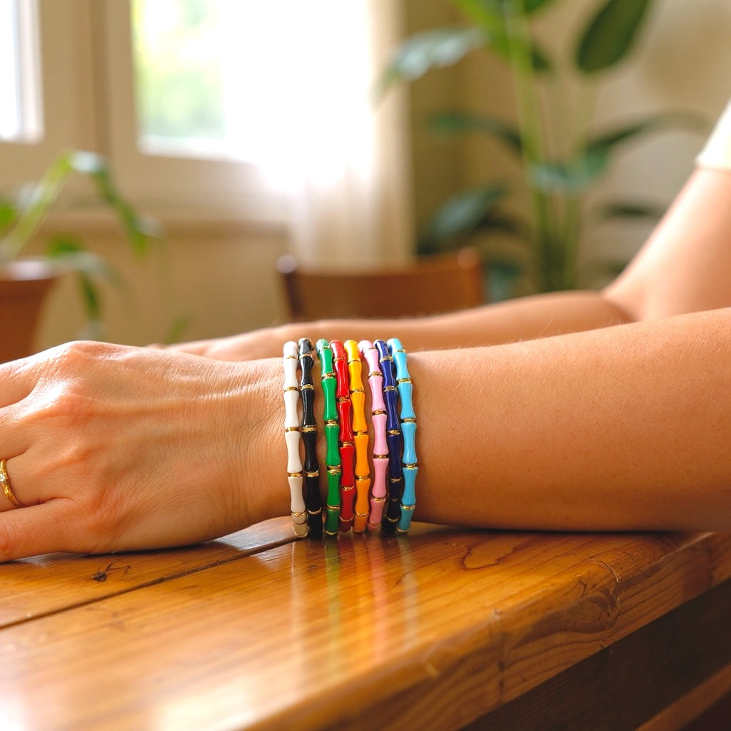 Lifestyle photo of a tarnish resistant gold bamboo style bangle with a baked enamel finish stacked with other everyday bracelets by Ashley Nicole Jewelry.