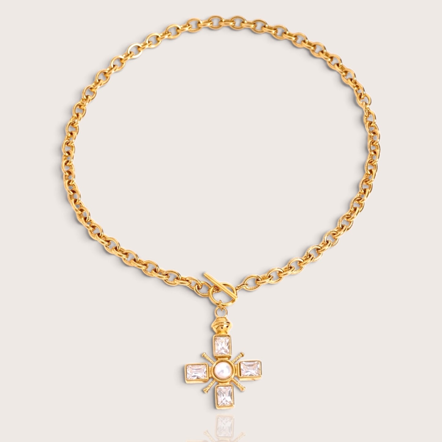 Flat lay Front view of a waterproof PVD gold over 316L stainless steel thick cable chain necklace featuring a decorative toggle clasp and a crystal-set Maltese cross pendant with a center pearl by Ashley Nicole Jewelry