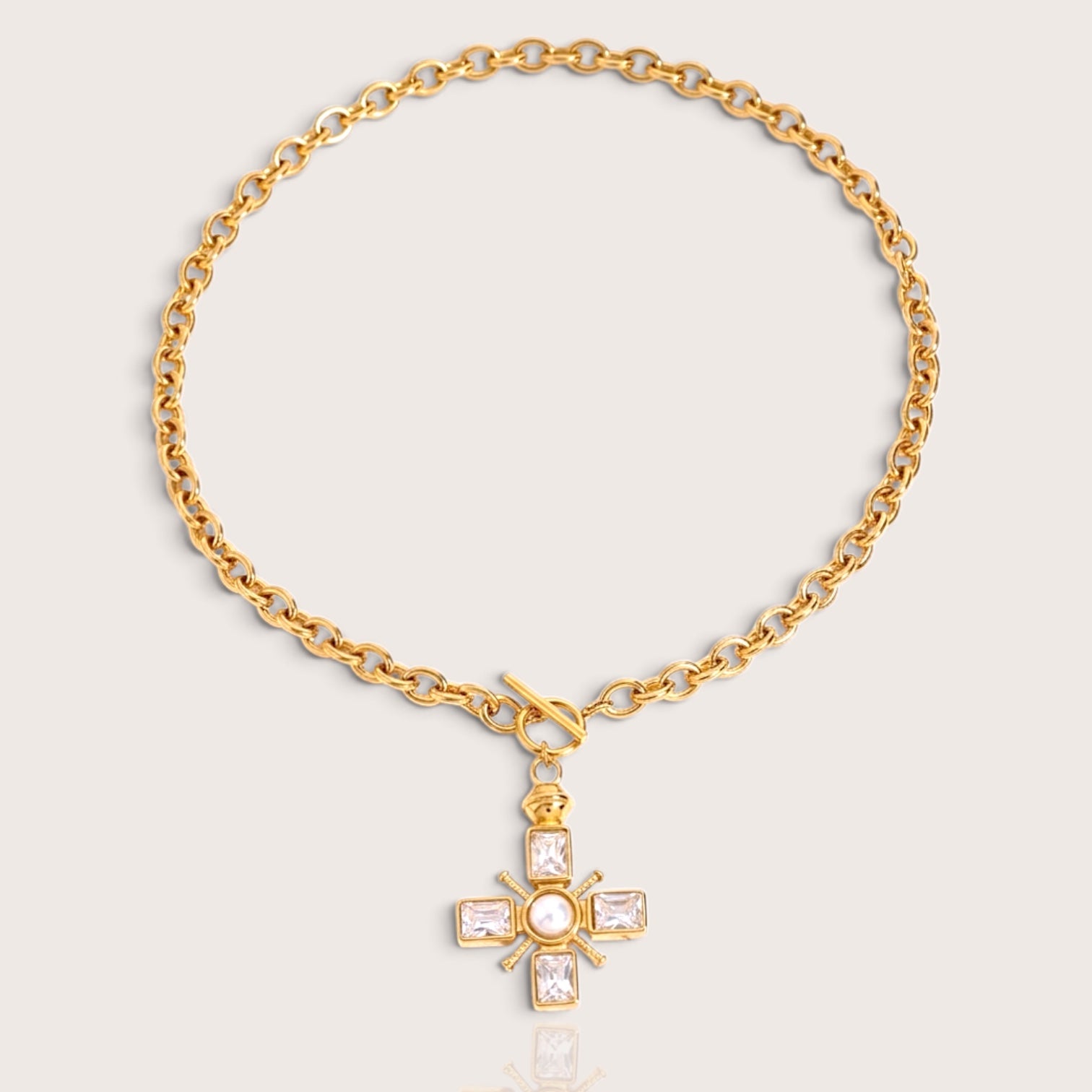 Flat lay Front view of a waterproof PVD gold over 316L stainless steel thick cable chain necklace featuring a decorative toggle clasp and a crystal-set Maltese cross pendant with a center pearl by Ashley Nicole Jewelry