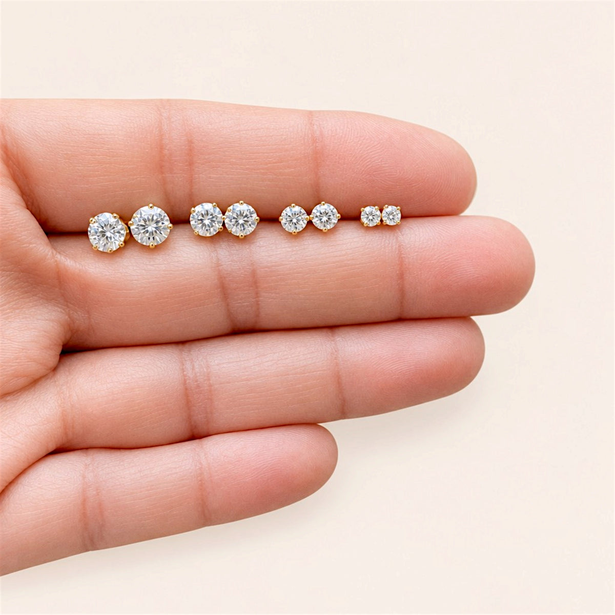 Four pairs of gold-filled CZ stud earrings arranged across fingers from largest to smallest.