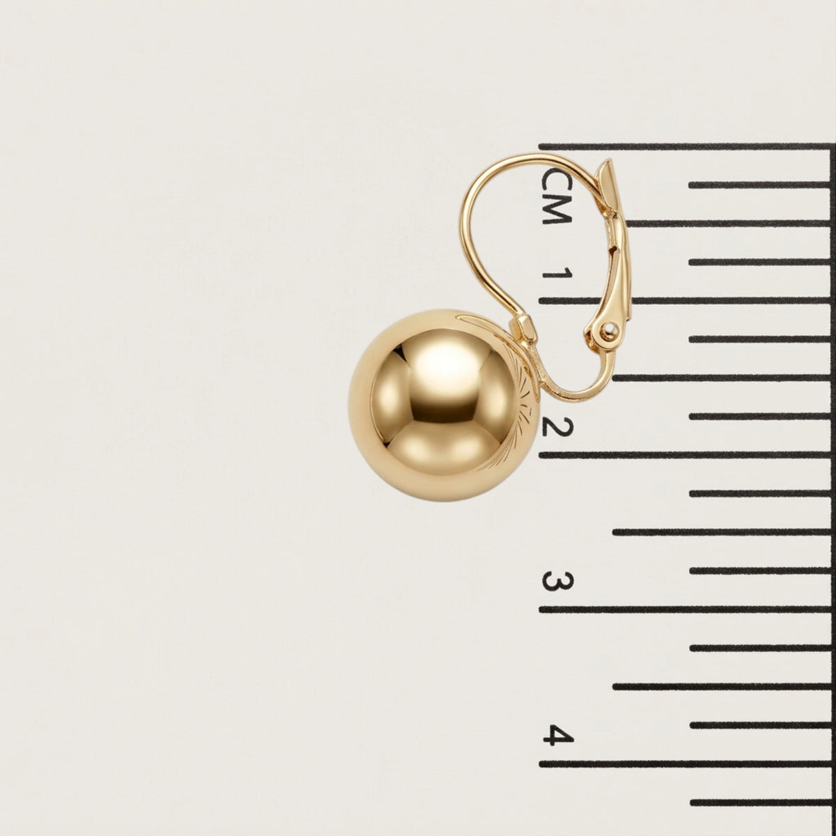 Single gold ball drop earring beside a centimeter ruler, showing its rounded shape and hinged lever-back closure.