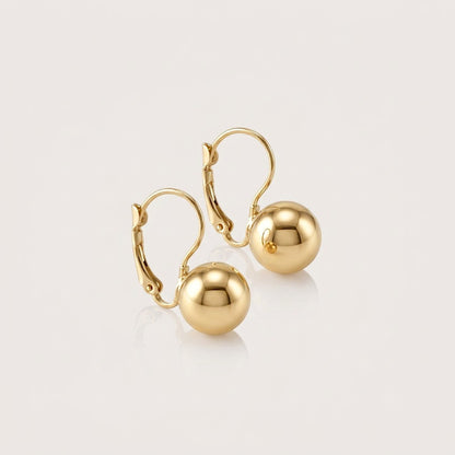 Pair of polished gold ball drop earrings with curved lever-back closures, arranged diagonally on a neutral background.