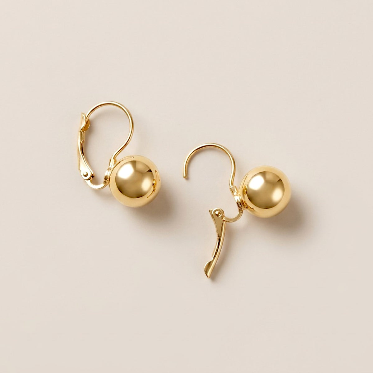 Two gold ball drop earrings shown with one lever-back closure open and the other closed