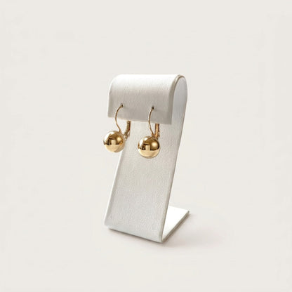 Pair of polished gold ball earrings hanging from a curved white jewelry stand on a neutral background.