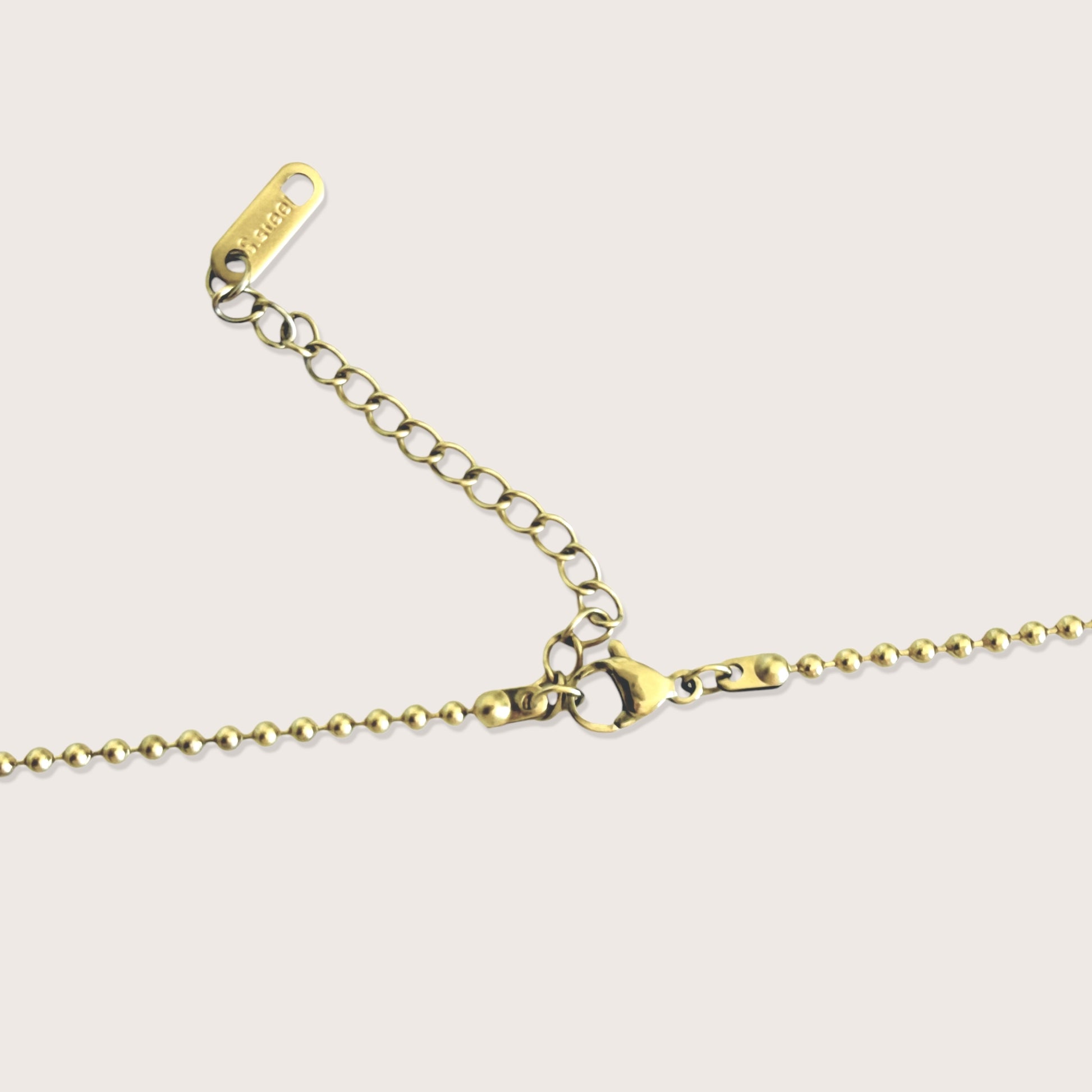 Rear view of the gold beaded ball chain showing the secure lobster clasp, the adjustment extender link, and the "ASHLEY NICOLE" branded tag.