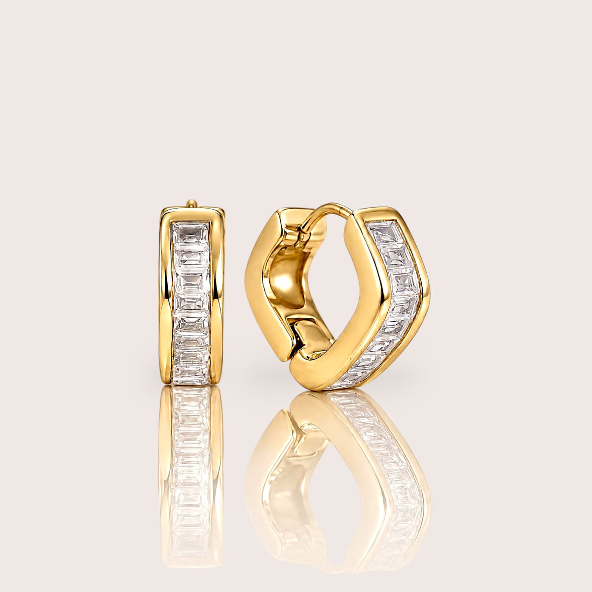 Gold hex baguette huggie hoop pair shown from the front and side on an ivory surface with soft reflections.