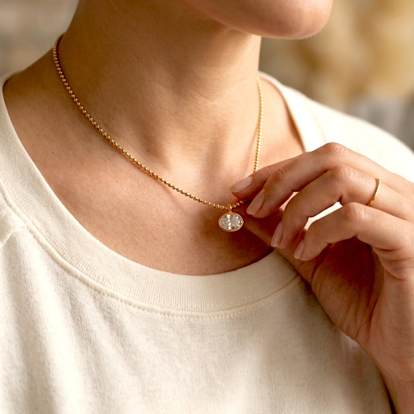 Model wearing the 18K gold horizontal oval bezel CZ necklace, showing the delicate fit on the décolletage with a hand lightly touching the pendant
