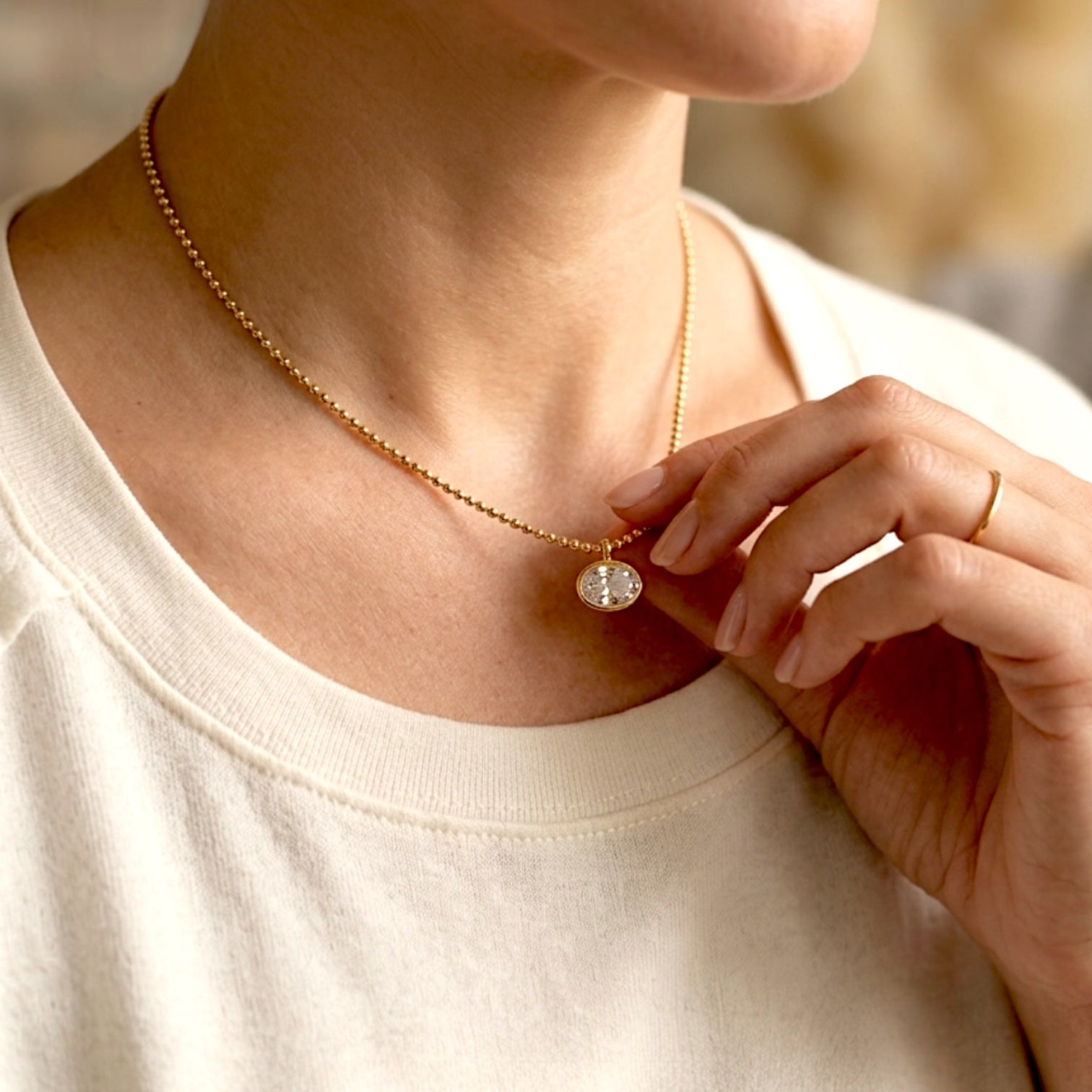 Model wearing the 18K gold horizontal oval bezel CZ necklace, showing the delicate fit on the décolletage with a hand lightly touching the pendant