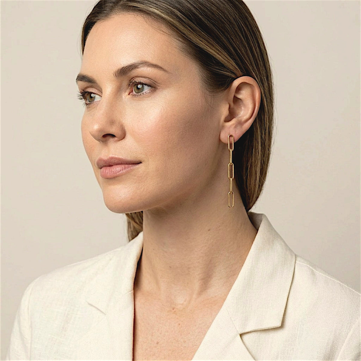 Model in an ivory jacket wearing gold filled paperclip dangle earrings, with her hair tucked behind her ear.
