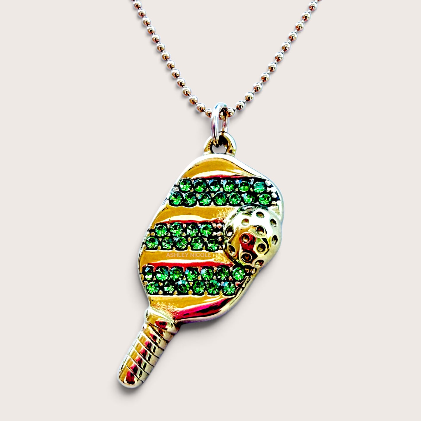 Close-up studio shot of the gold pickleball paddle pendant with green pavé cubic zirconia on a beaded ball chain.