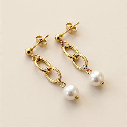 Two gold link pearl drop earrings arranged diagonally on a neutral surface, with the posts and butterfly backs visible.