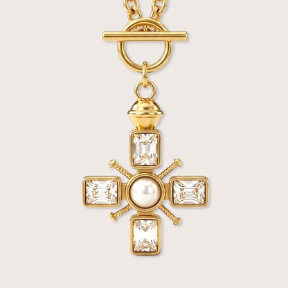 Macro close-up view of the architectural gold Maltese cross pendant detailing bezel-set emerald-cut crystals and a central pearl accent.