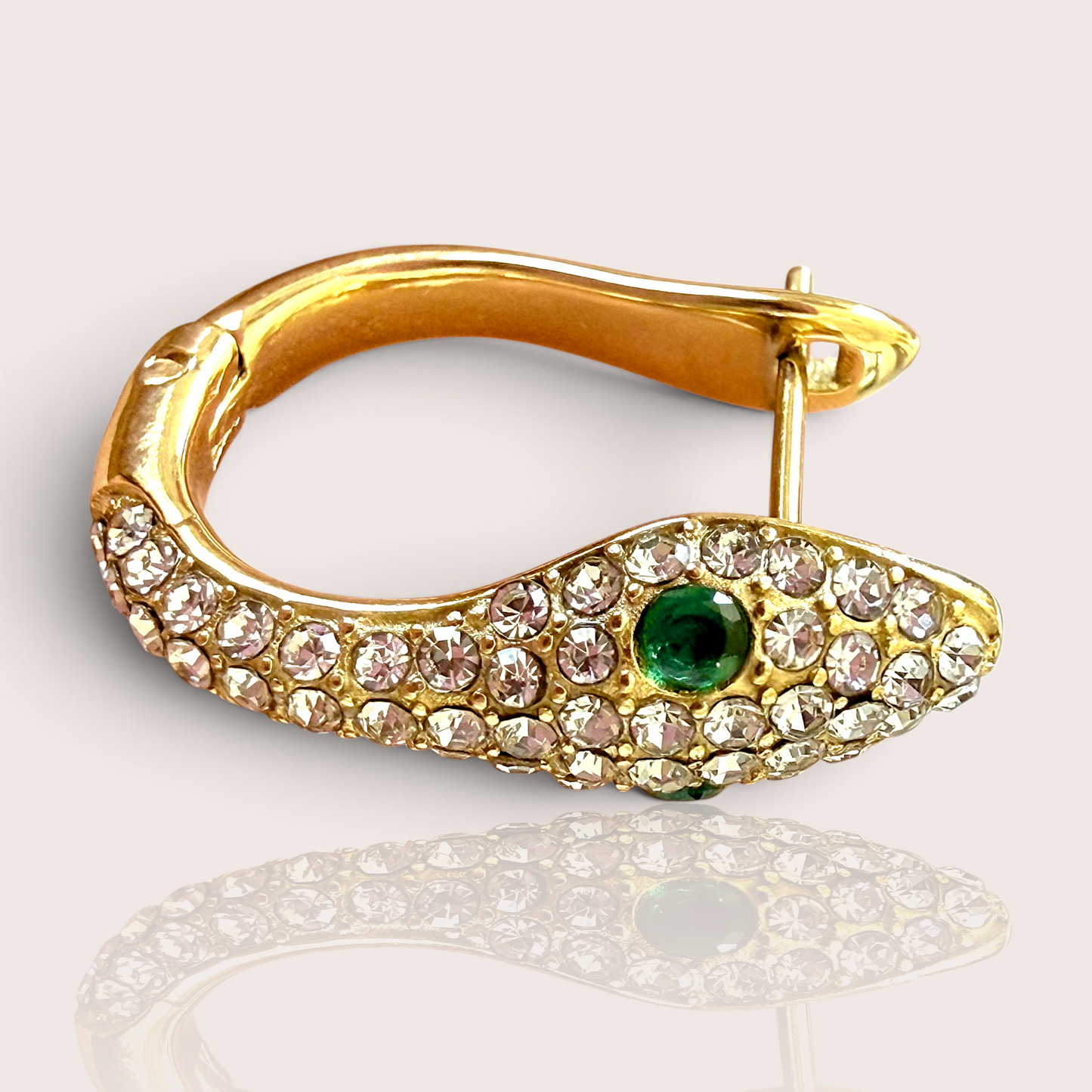 A single 18K gold PVD-finished snake huggie earring, encrusted with clear zircons and featuring a single vivid green crystal eye, shown lying flat with a slight reflection.