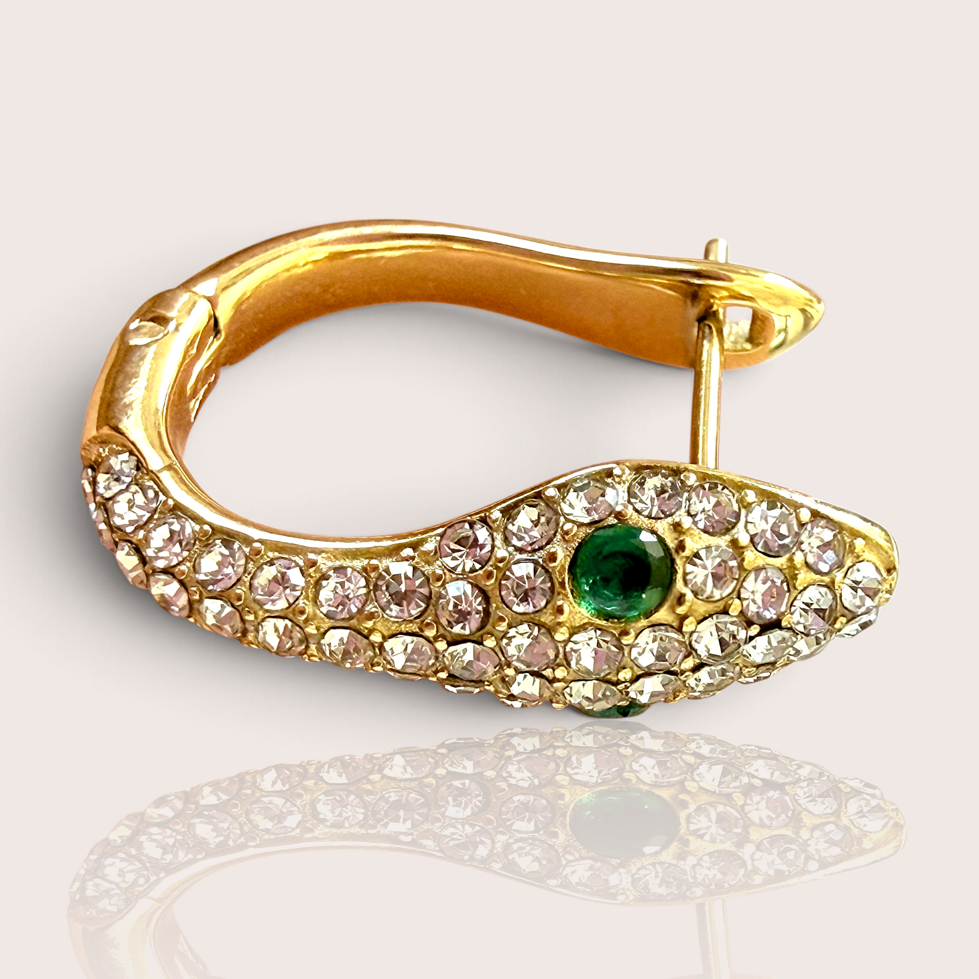 A single 18K gold PVD-finished snake huggie earring, encrusted with clear zircons and featuring a single vivid green crystal eye, shown lying flat with a slight reflection.