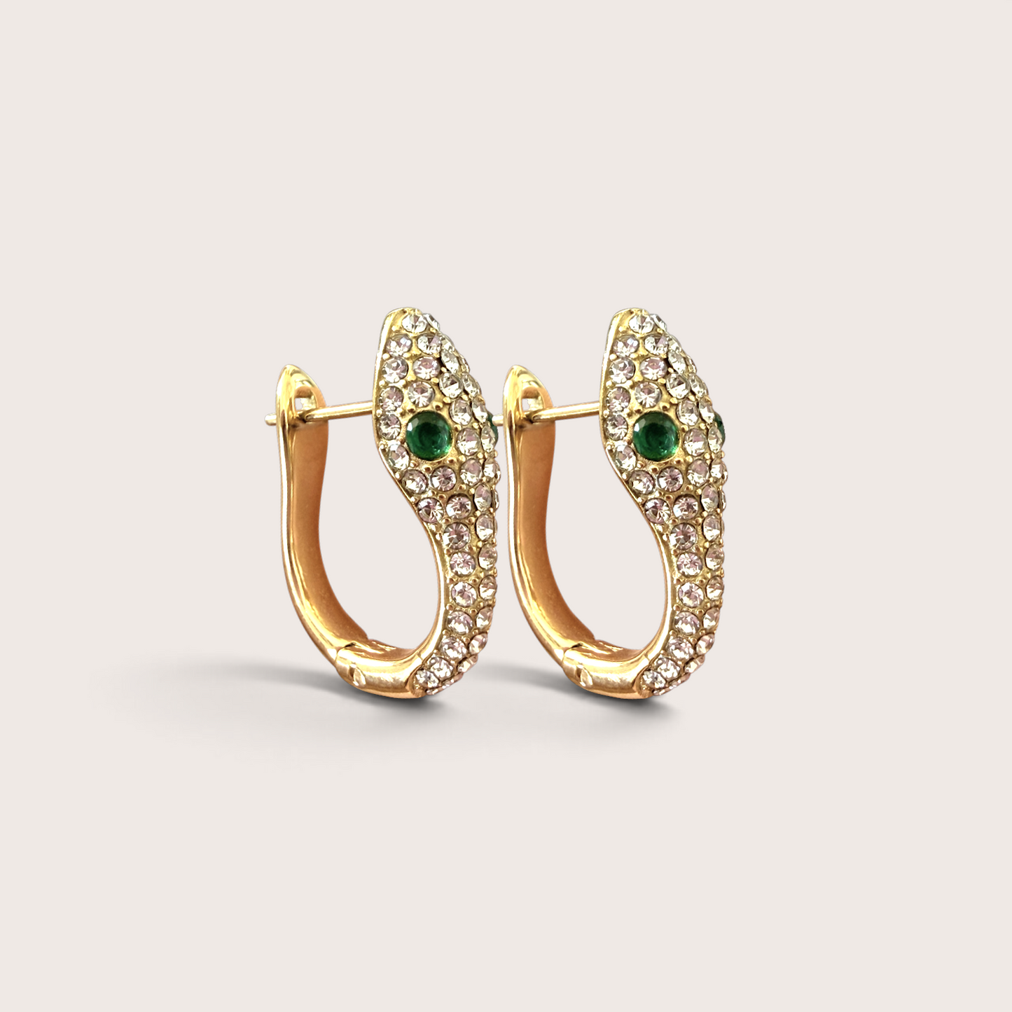 Pair of 18K gold PVD-finished snake huggie earrings encrusted with clear zircons and green crystal eyes, studio view on a neutral background.