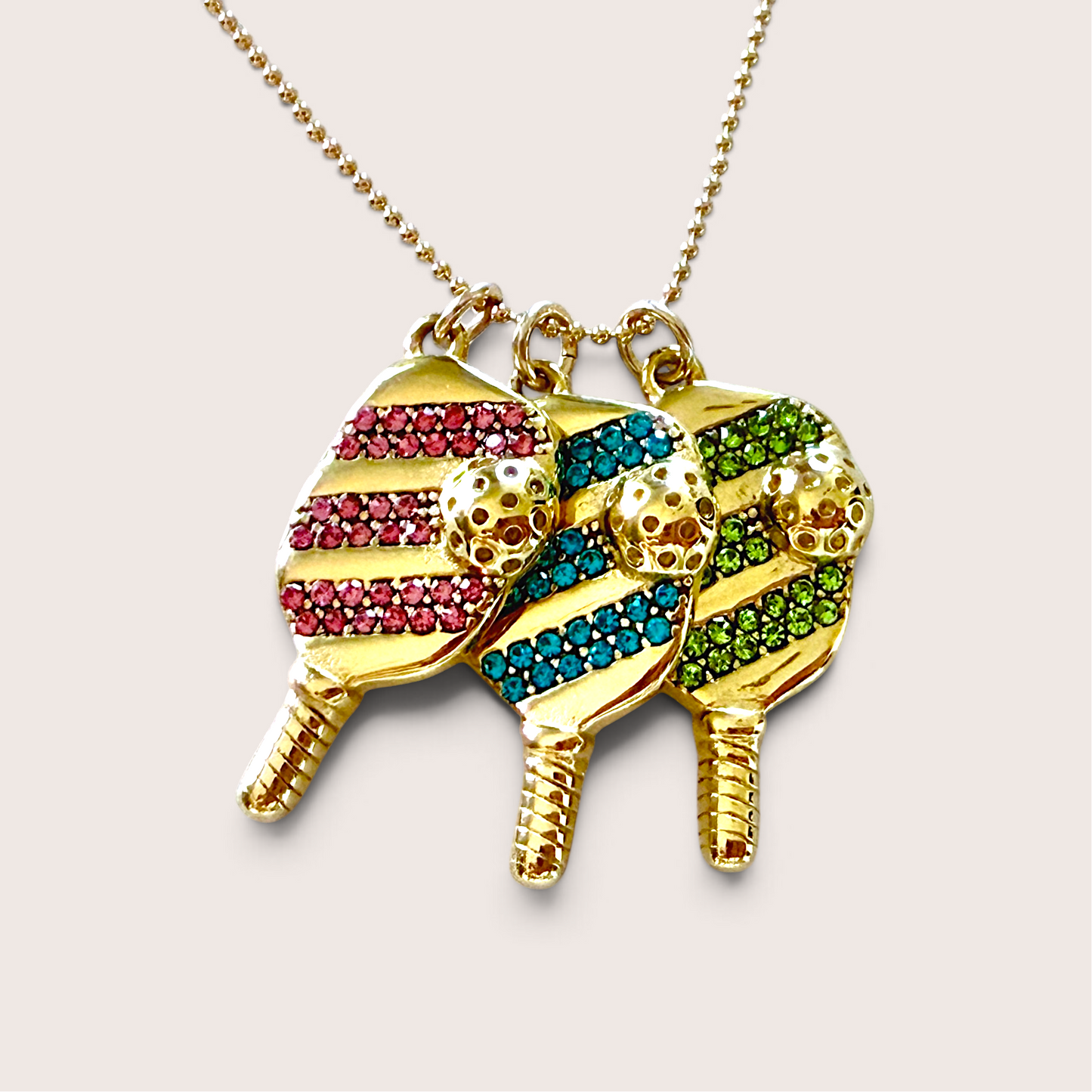 Gold pickleball necklace featuring three multi-color paddle charms displayed together on a plain background