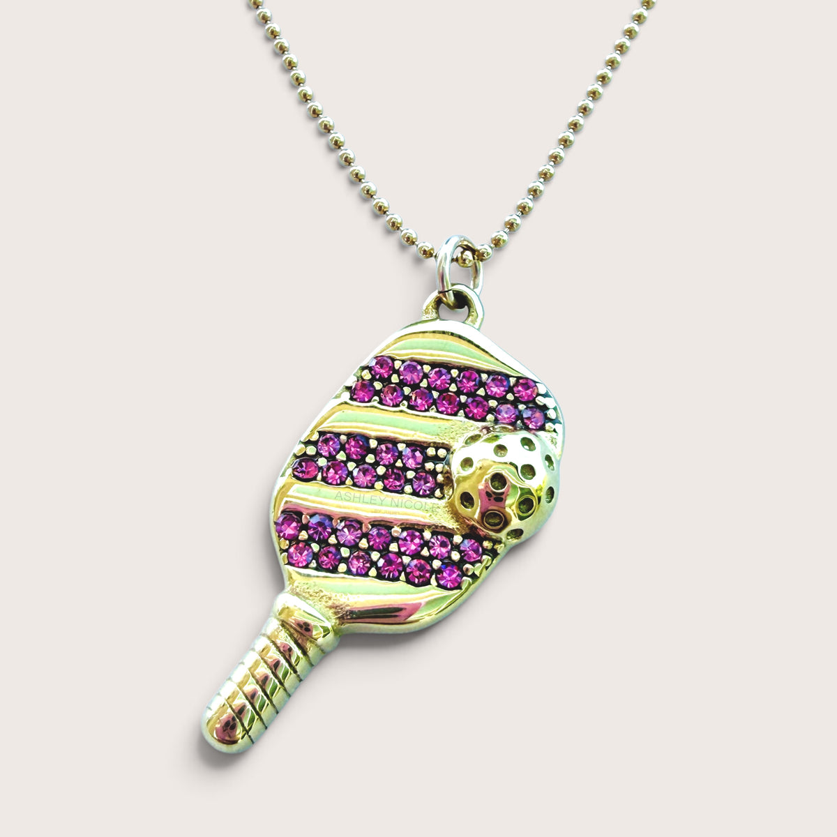 Close-up studio shot of the gold pickleball paddle pendant with pink pavé cubic zirconia on a beaded ball chain.
