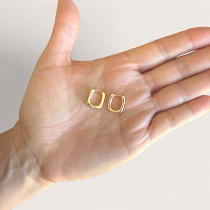 Pair of small gold rectangular huggie earrings resting in an open palm to show their relative size.